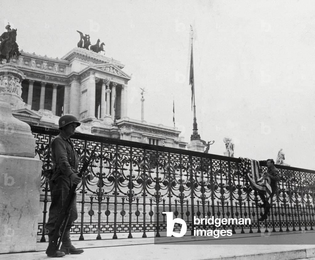 An Italian soldier takes down the U.S. flag hoisted in front of the Altare della Patria, in Rome, on liberation day. In the foreground to the left, a sentry