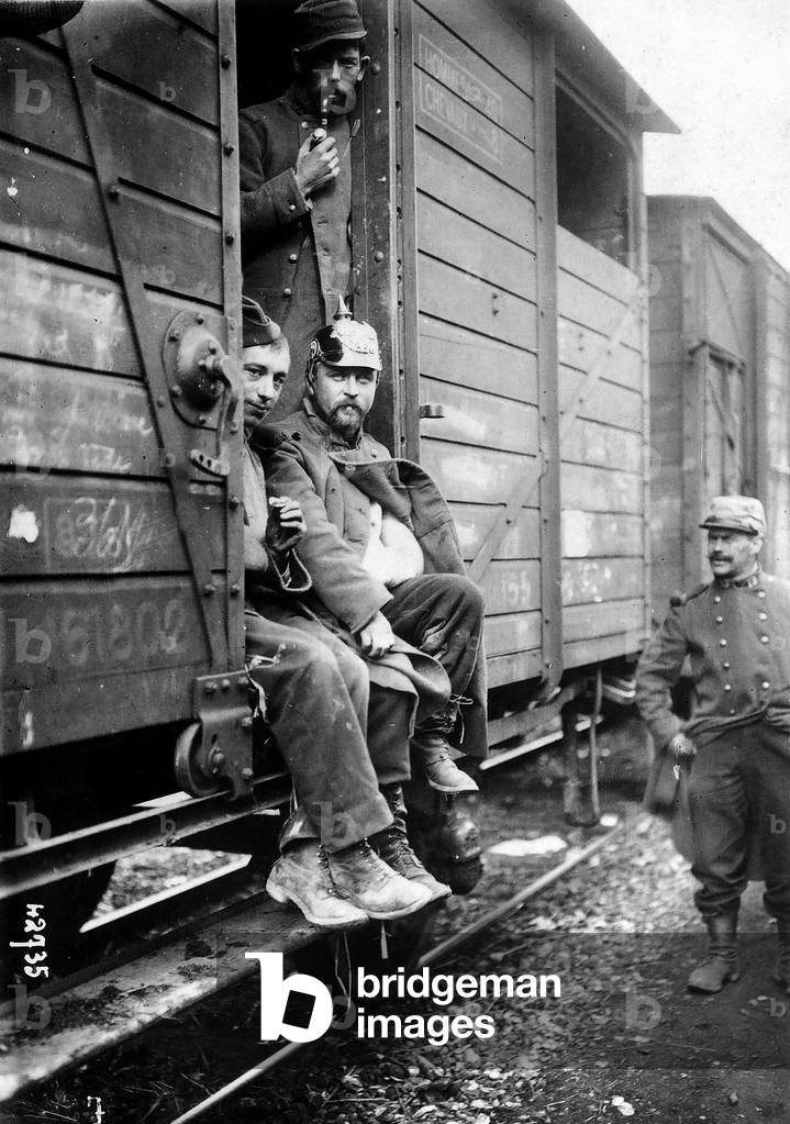 Arrival of a French wounded-troop convoy. Three soldiers appear in the entrance of a car, while a third stands up near the train. (b/w photo)