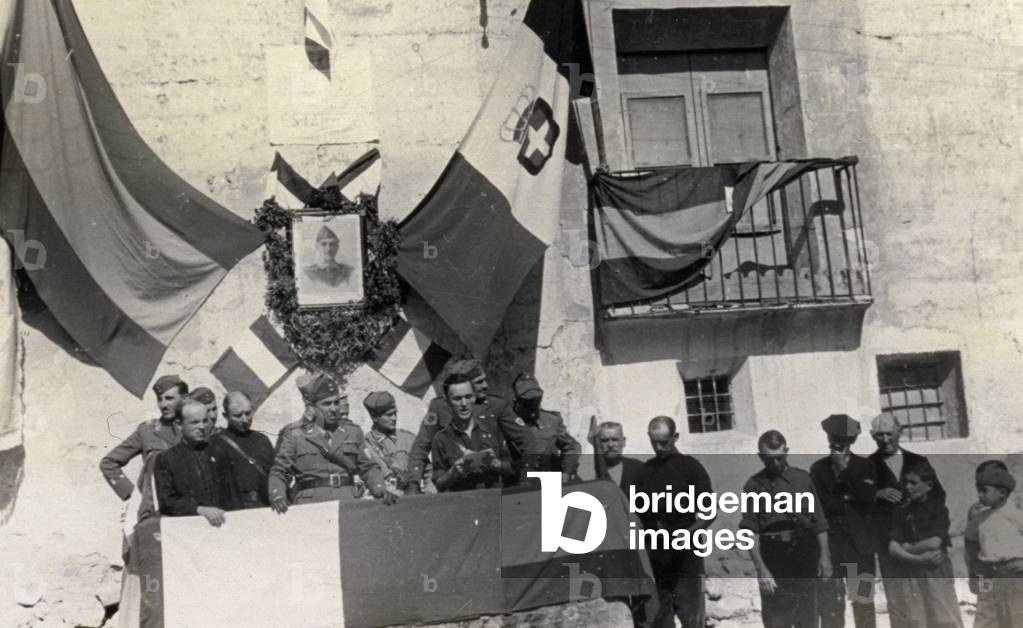 Snapshot during the manifestaion for the day of the Caudillo in Alba in 1938, during the Spanish civil war. A group of military, one of whom is speaking to the public, are on a small stand behind which the Spanish and Italian flags are displayed. On the right, a few men and children are listening (b/w photo)