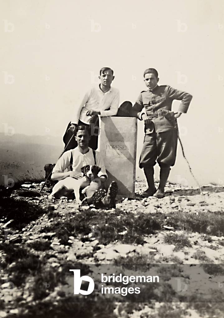 Three men and a dog photographed near a boundary stone, on top of Monte Porozen, at the Italian-Slovenian border.