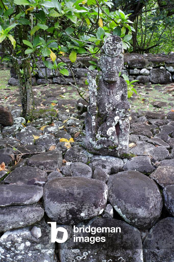 Paepae (surelevee platform serving as a terrace and floor for dwellings) adorns a modern tiki representing a great warrior holding a victim/archeological site of Hikokua in the Hatiheu Valley/Nuku Hiva Island/Marquises Archipelago/French Polynesia