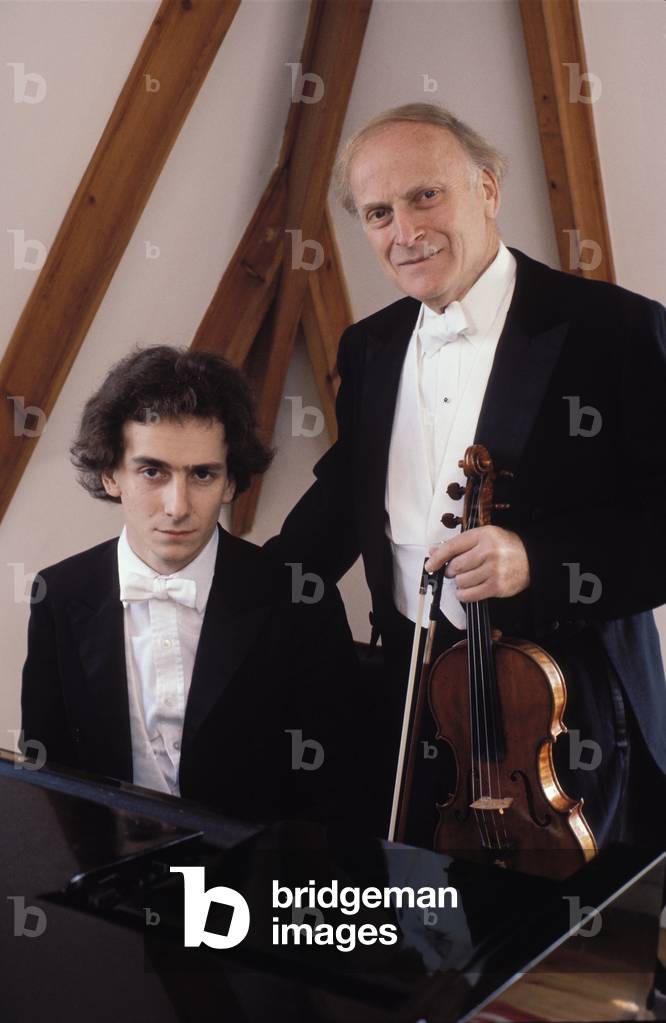 Yehudi Menuhin holding violin with his son Jeremy seated at piano, circa 1974