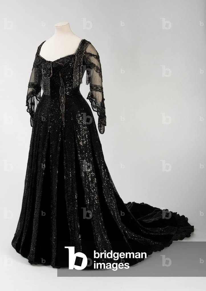 Black full length evening gown worn by Queen Alexandra, with bead and sequin decoration and incorporating Queen Alexandra’s signature black silk and gold lettered name tape, made by Barolet of Knightsbridge, London 1908-1910 (silk & velvet)