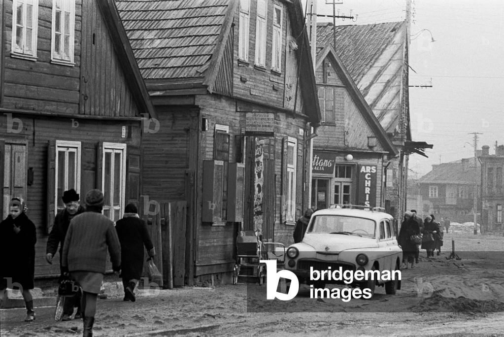 Bialystok, Poland, 02.1971. Passers - by and wooden houses along a non tar street in the city. 