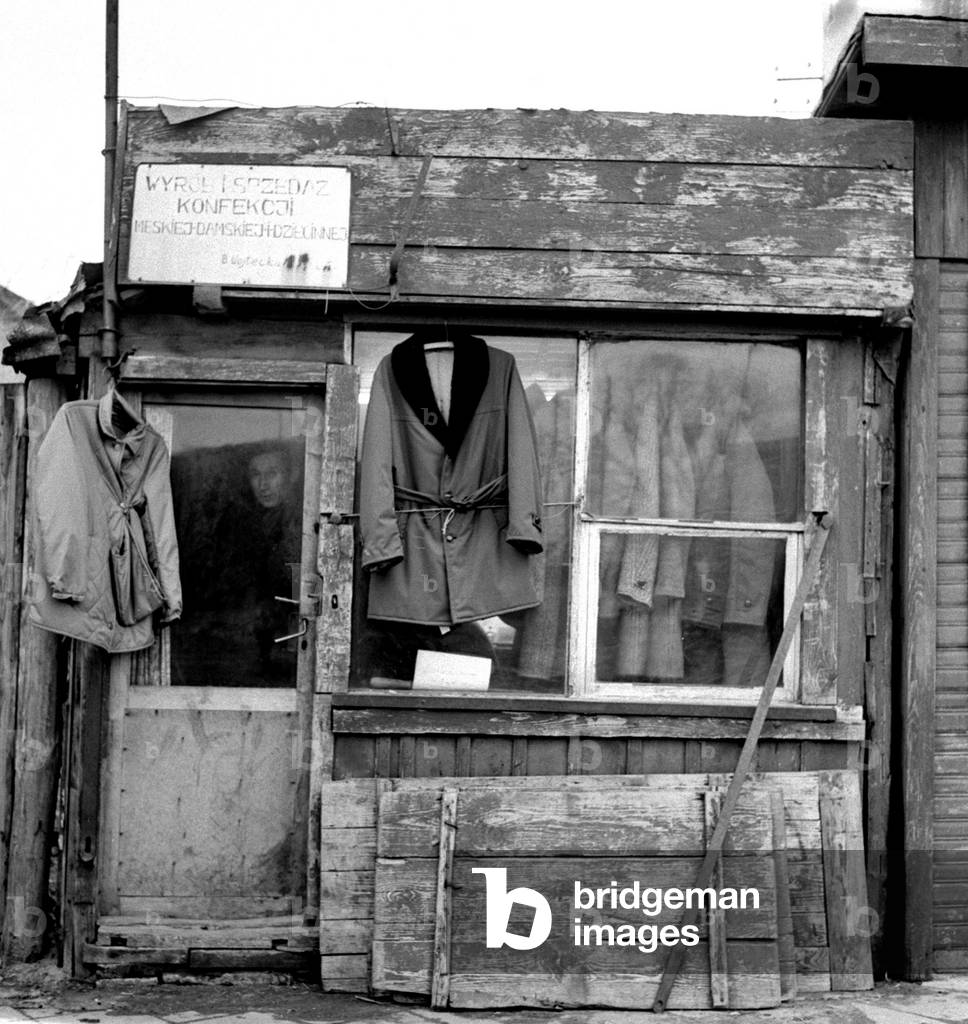Bialystok, Poland, 02.1971. Little clothes shop. Man in the window is a craftsman sewing and selling clothes both for men and women. 