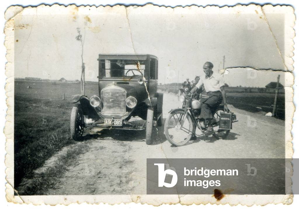 Ejszyszki, Lida County; Nowogrzodzkie Voivodeship, inter-war period Poland, (present day Lithuania),1930s. Man on motorbike next to one of the first auto mobiles in Ejszyszki. Picture from Zofia Wieckiewicz's family album. 