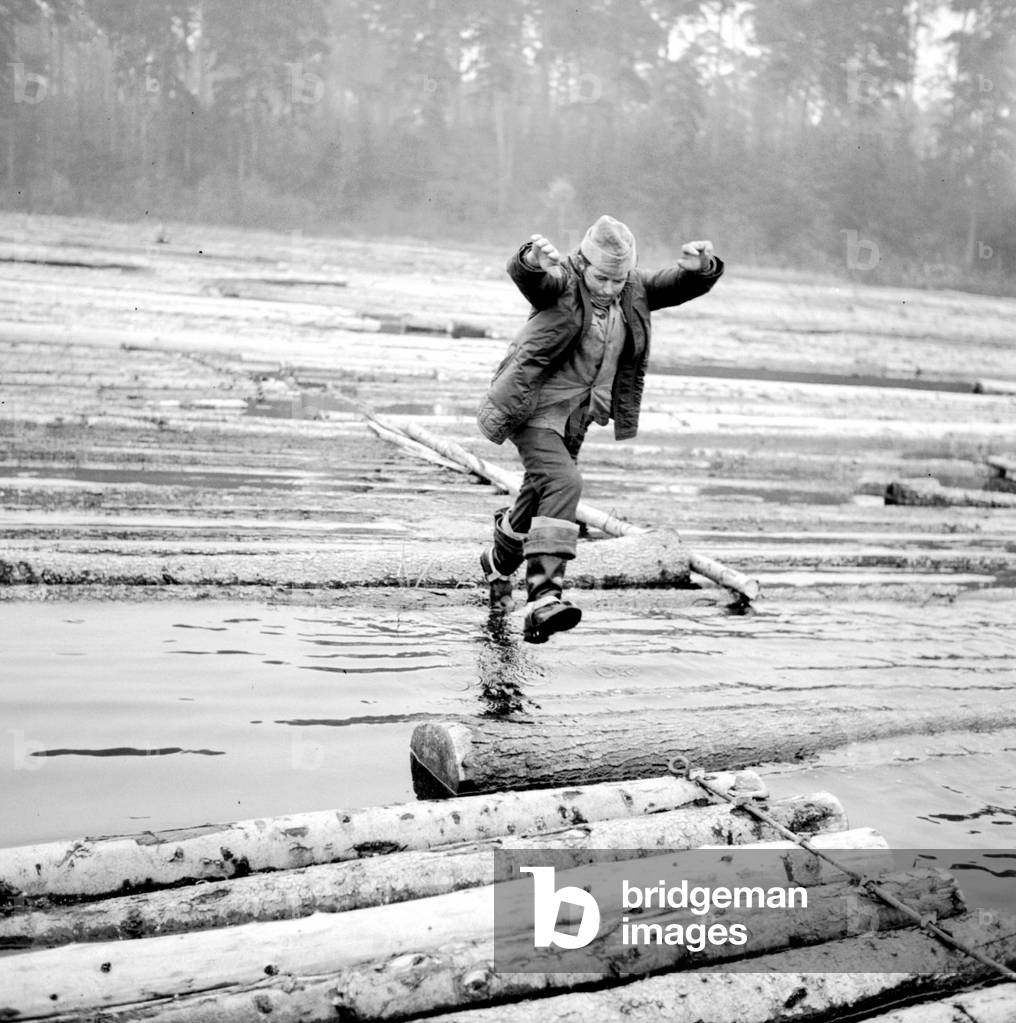 Bialystok region, Poland, 1973, Pieces of wood transported by river. Rafts man jumping over floating blocks of wood. 