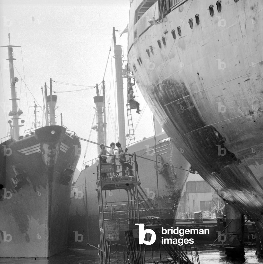 Swinoujscie and Szczecin, Poland, 1979. Workers painting board of ship in the seaport. 