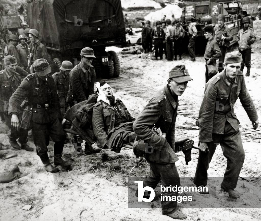 German prisoners on the beach Ruquet in Saint-Laurent-sur-Mer carry one of their soldiers on a stretcher, Saint-Laurent-sur-Mer, Normandy, France, June 1944 (b/w photo)