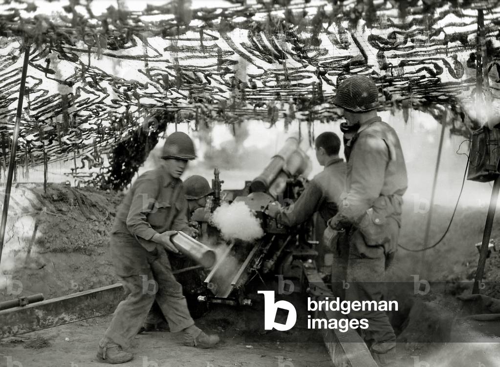 A 105 mm HM2 howitzer in action under a camouflage netting, Saint-Lô, Normandy, France, July 1944 (b/w photo)