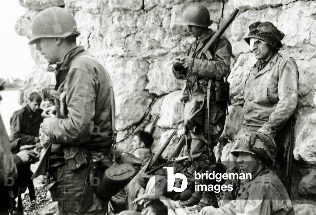 Soldiers from the 1st Infantry Division are protected from German fire at the foot of the cliff of Colleville-sur-Mer, Omaha Beach, Normandy, France, 6th June 1944 (b/w photo)