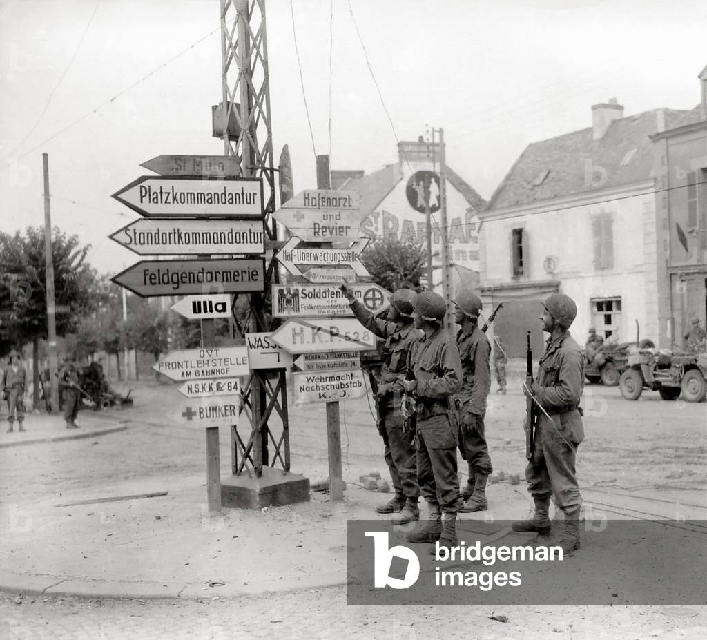 Four GI's at the crossroads have fun reading German signs that indicate the direction of the barracks, headquarters staff, military police, shelters, aid stations and other positions, Place Poincaré Paramé (now a district of Saint-Malo) near Boulevard Rochebonne, Paramé, Normandy, France, 10th August 1944 (b/w photo)