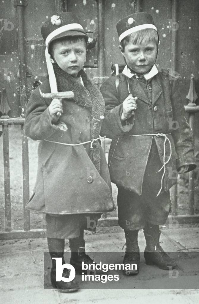 Two small boys wearing military hats and carrying homemade swords, London, 1918 (b/w photo)