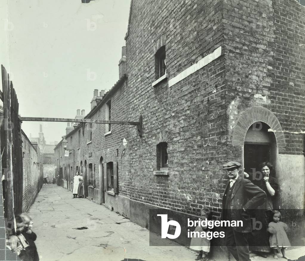 Little Britain, Tabard Street: family outside slum housing, 1913 (b/w photo)