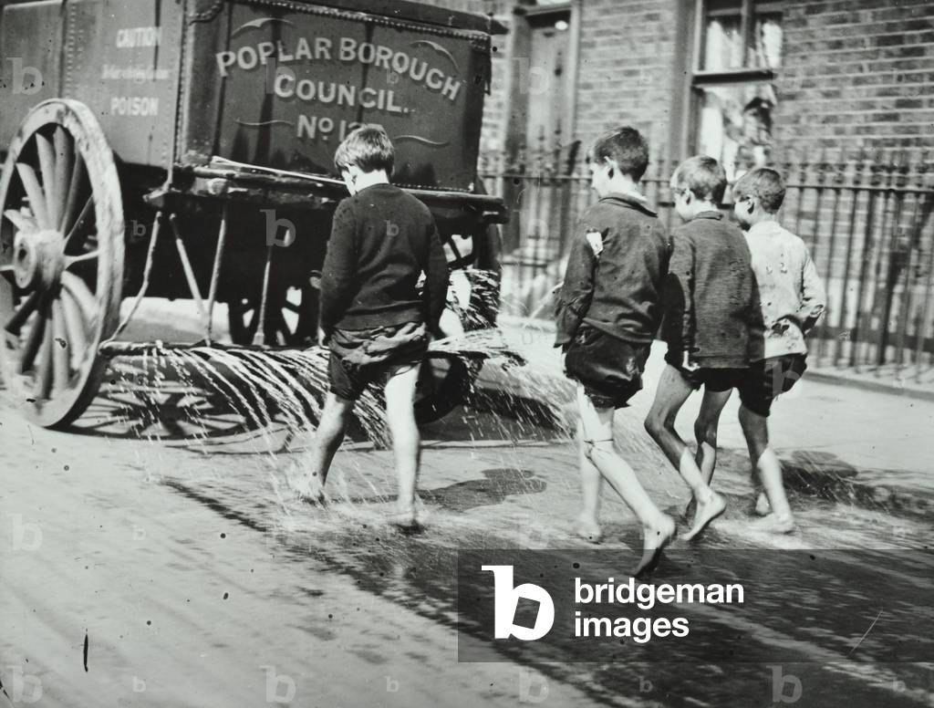 Boys following a water cart in Cotton Street, London, 1910 (b/w photo)