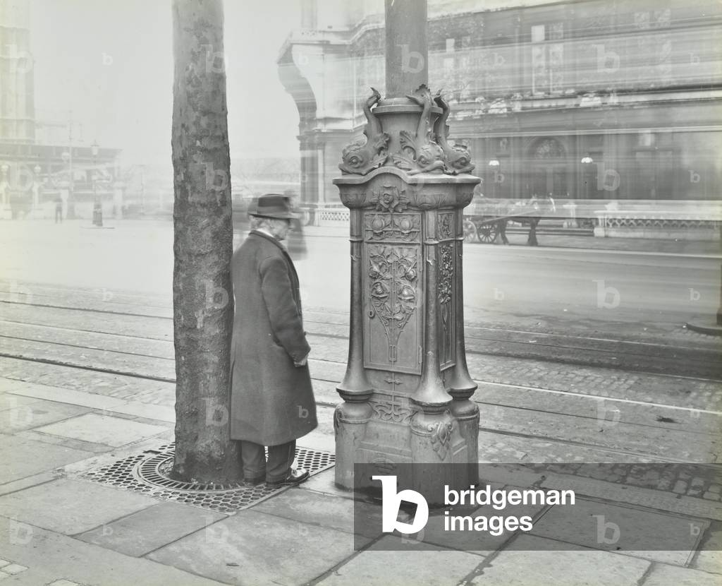 Man stood next to an ornated electric lighting standard, Victoria Embankment, 1932 (b/w photo)
