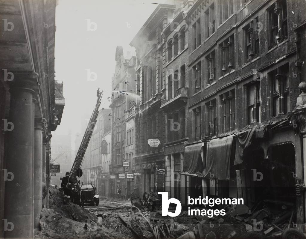 View of Old Bailey looking towards Ludgate Hill showing bomb damage including a bomb crater in the foreground. In the background a firefighter on a fire engine ladder turns a hose on a burning building, 1941 (b/w photo)