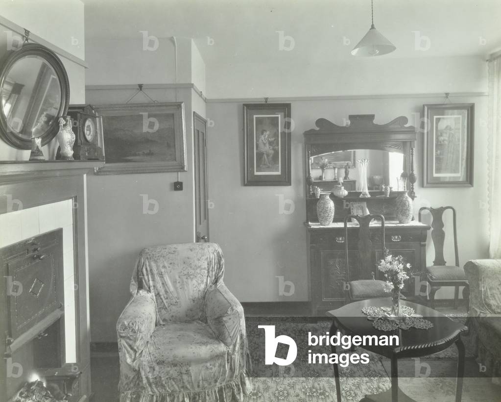 East Hill Estate: interior of tenement, showing armchair, table, mirror and cabinet, London, 1925 (b/w photo)