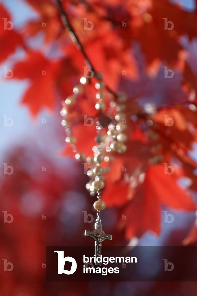Rosary cross hanging on a tree branch with red leaves. Autum.  France.