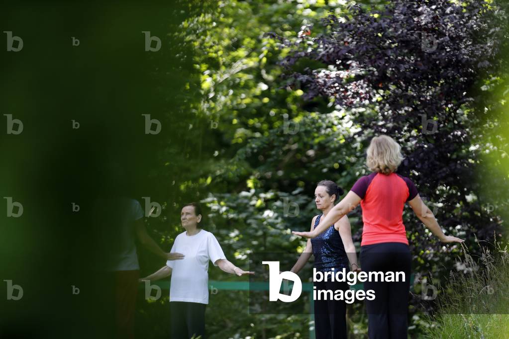 Women practicing Qi Gong or Tai Chi exercise in a wellness course in nature.  France.