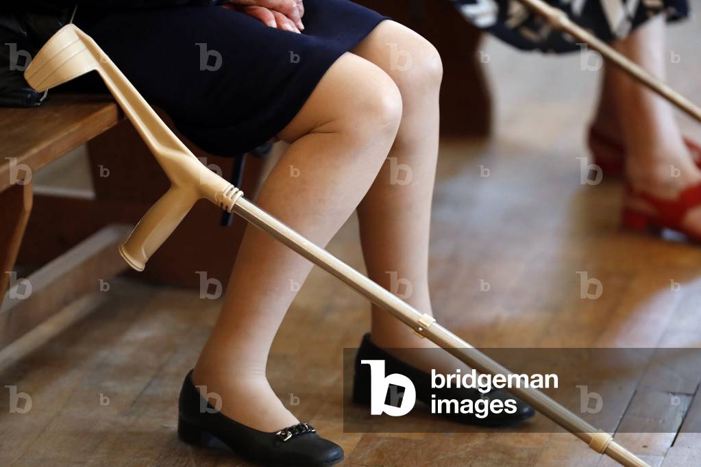 Elderly woman with crutch at sunday catholic mass.  France.