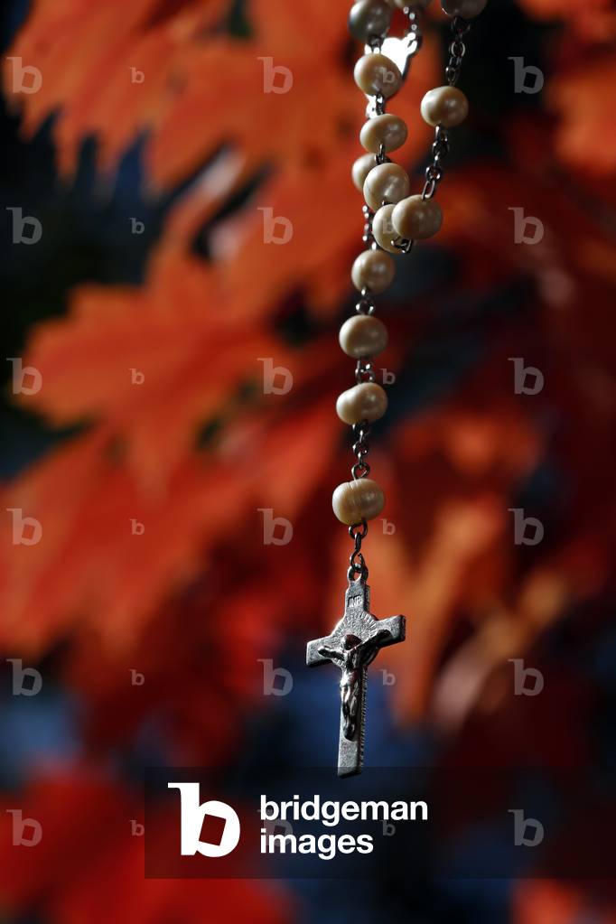 Rosary cross hanging on a tree branch with red leaves. Autum.  France.