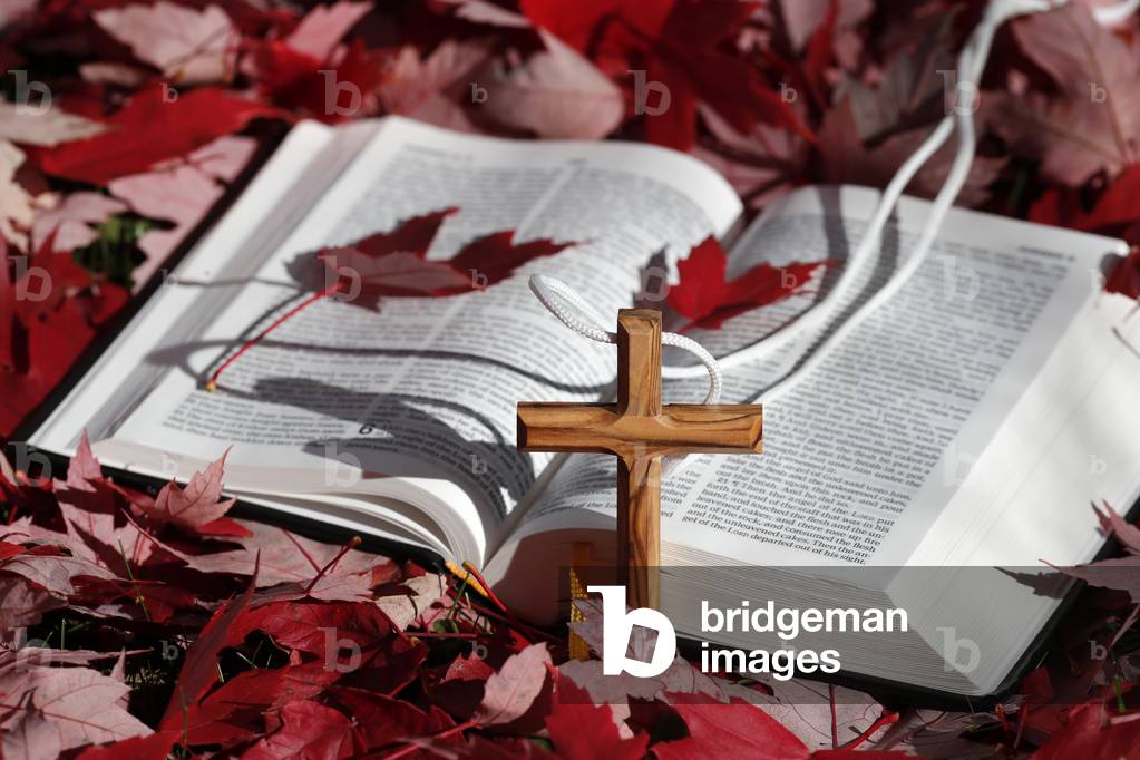 Bible and christian cross on dry fallen autumn leaves. Faith and spirituality. France.