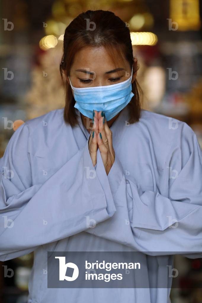 Tu An Buddhist temple. Woman praying  with surgical mask at buddhist ceremony. Covid-19.  France.