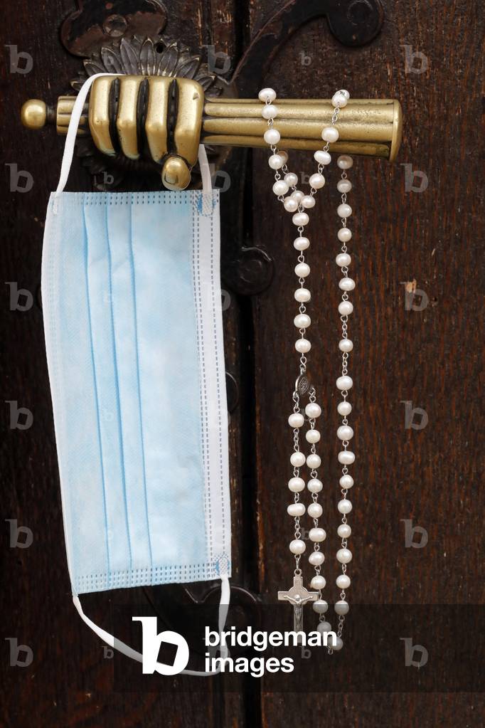 Old metal church door handle. Blue Surgical mask and Rosary.  Covid-19 epidemic.  Sanctuary of La Benite Fontaine. France.