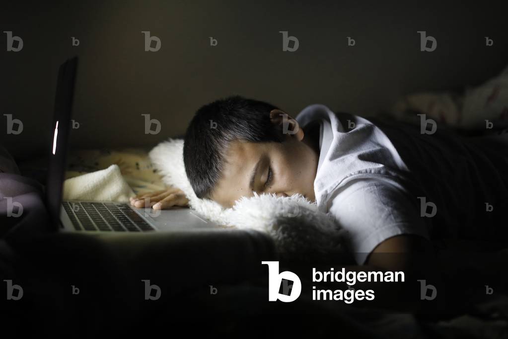 Boy falling asleep in front of a computer screen at night in Montrouge, France
