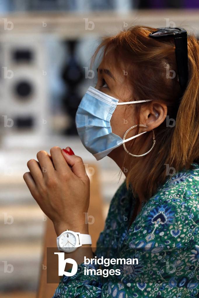 Woman with  surgical mask praying in church during coronavirus epidemic. Covid-19.