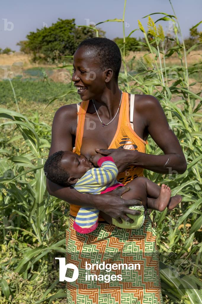Mother feeding her baby while working in a field near Dapaong, Togo.