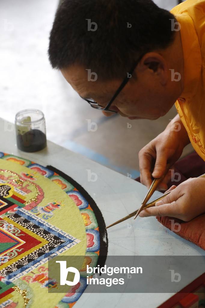 Tibetan Monk carefully works on a colorful Sand Mandala (photo)