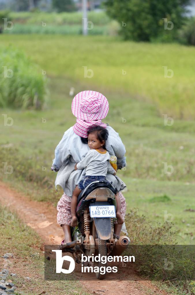 Mother and daughter on motorbike in the countryside, Kep, Cambodia (photo)