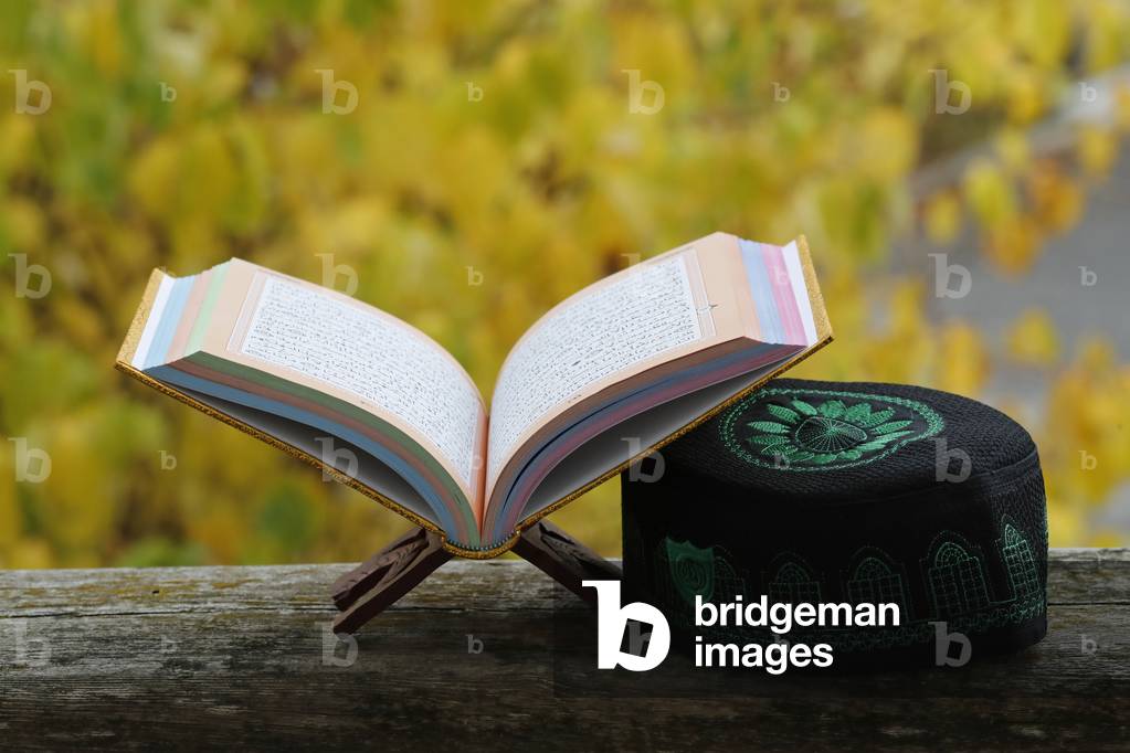 An open Holy Quran  on wood stand  and a kufi.  France.