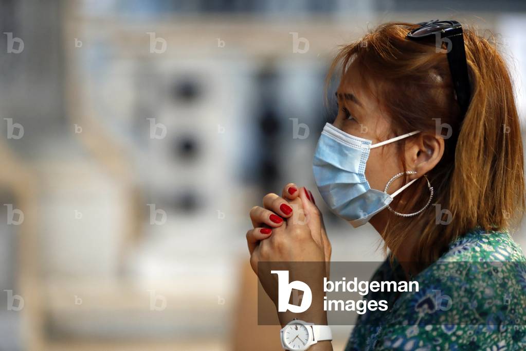 Woman with  surgical mask praying in church during coronavirus epidemic. Covid-19.