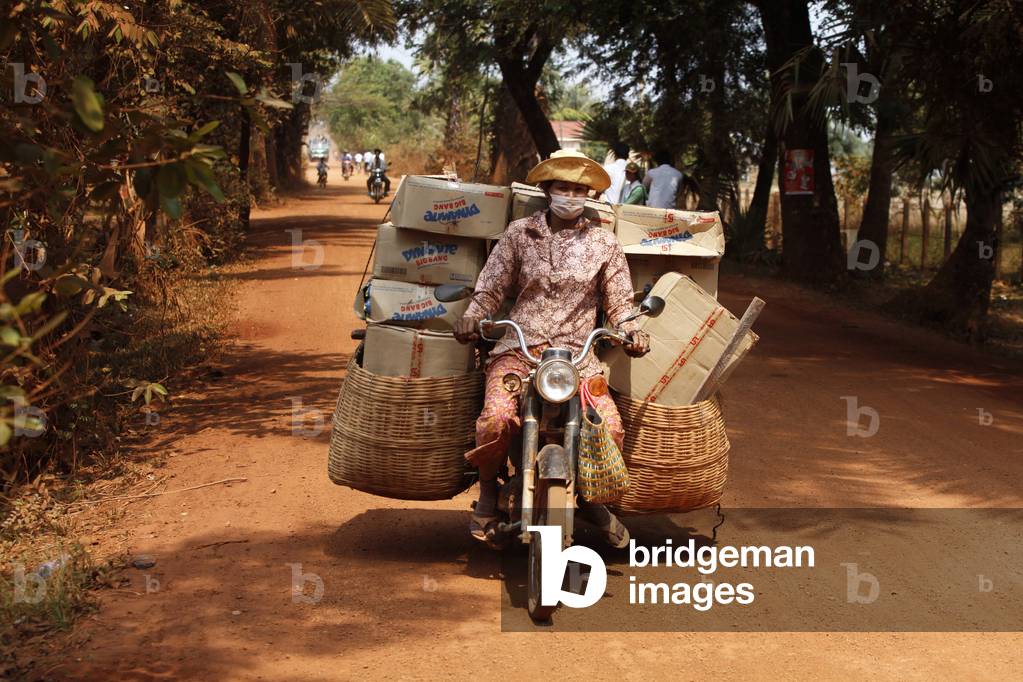 Woman transporting goods on a dirt road Cambodge
