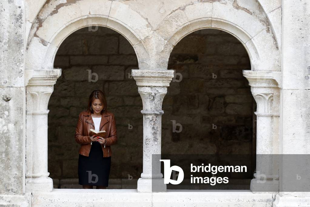 Cistercian Abbey of Fontenay.  Woman reading the bible in the cloister.  France.