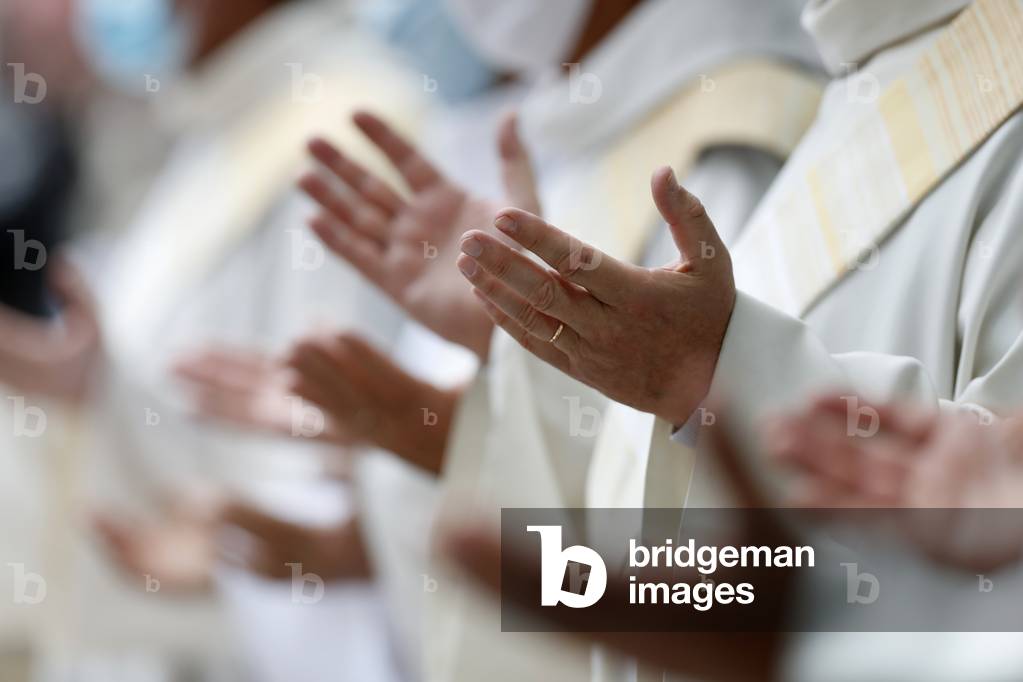 Catholic church during covid-19 epidemic.  Celebration of the mass.   Priests praying. Close-up on hands.  Sanctuary of La Benite Fontaine. France.