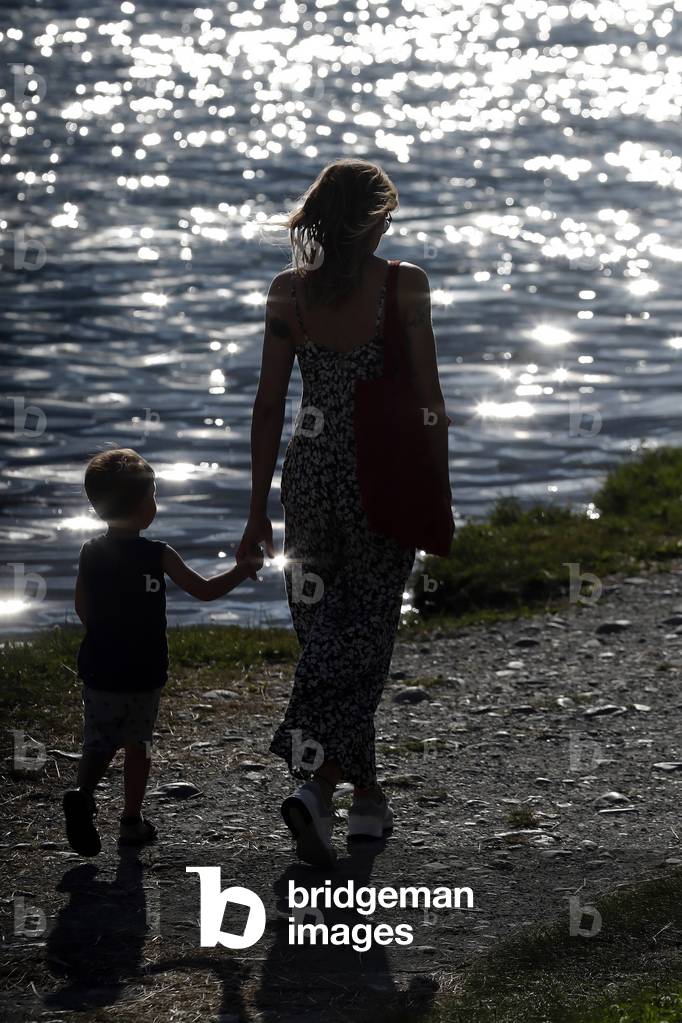 Woman and son walking by lake at sunset.   France.