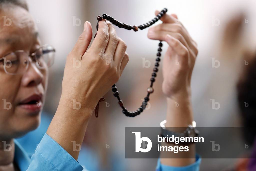 Hands of a woman holding a rosary or crucifix while praying, Christian daily devotional of a worshiper of God the Savior, Phu Cam Cathedral, Hue, Vietnam, 2019 (photo)