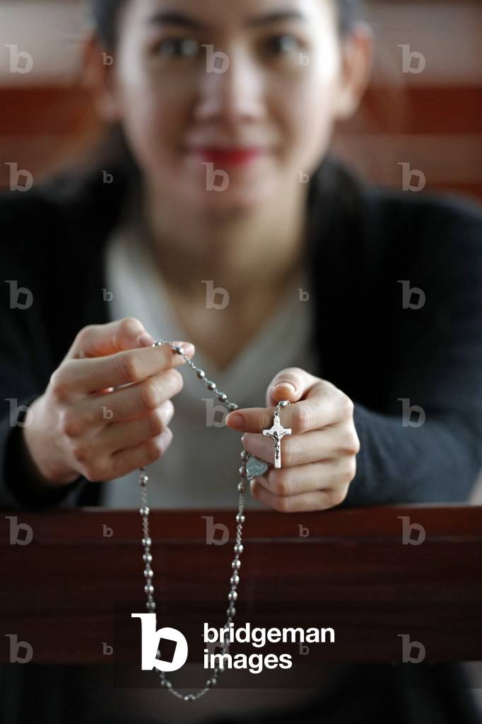 Hands of a woman holding a rosary or crucifix while praying, Christian daily devotional of a worshiper of God the Savior, Basilica of Our Lady of La Vang, Pilgrimage, La Vang, Vietnam, 2019 (photo)