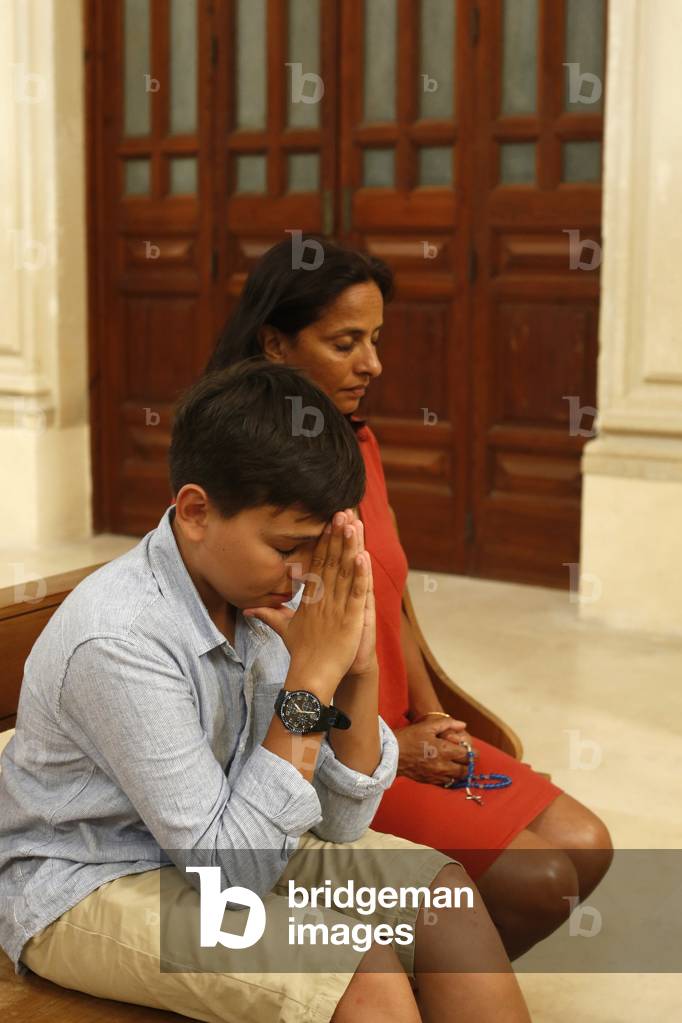 Mother and son praying and reading the bible in a church in Lecce, Italy, 2019 (photo)