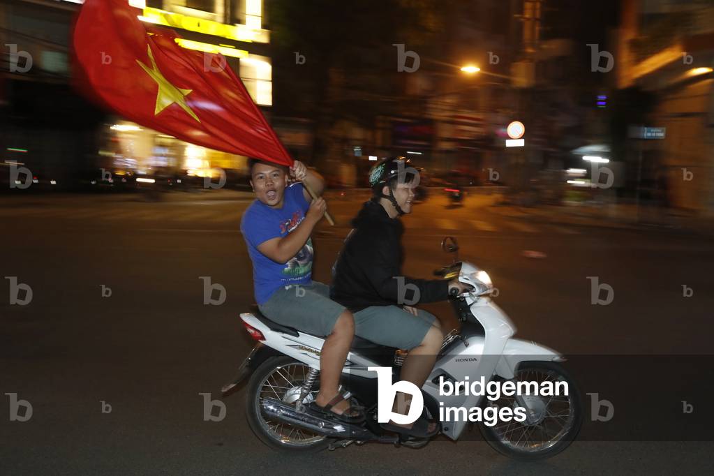 Vietnamese people driving a motorbike at night with vietnamese flag, Ho Chi Minh city, Vietnam (photo)