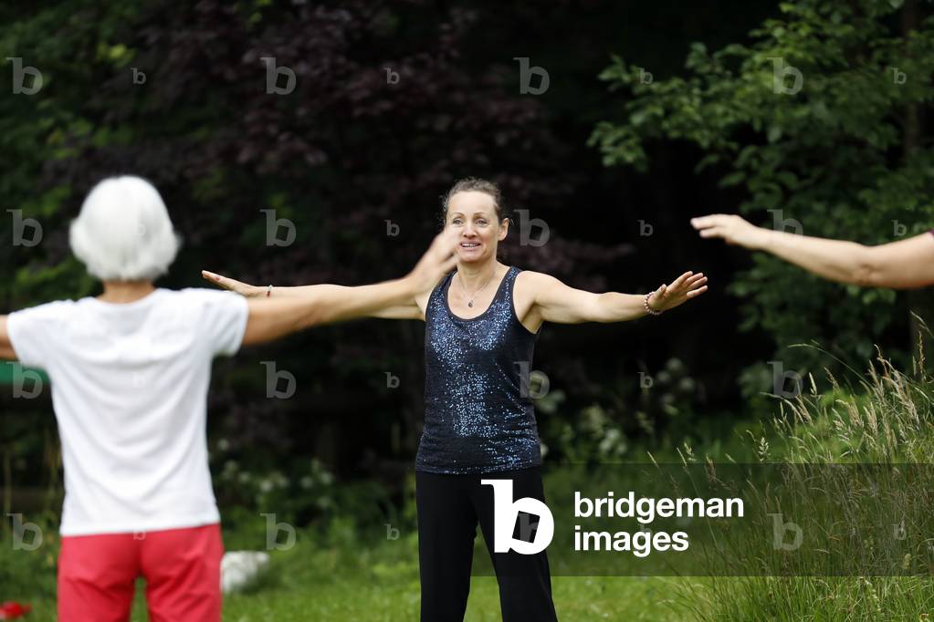 Women practicing Qi Gong or Tai Chi exercise in a wellness course in nature.  France.
