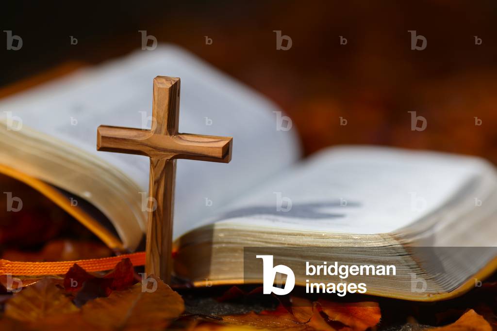 Open bible and christian cross on dry fallen autumn leaves. Faith and spirituality.  France.