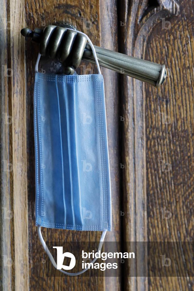 Old metal church door handle. Blue Surgical mask. Covid-19 epidemic.  Sanctuary of La Benite Fontaine. France.