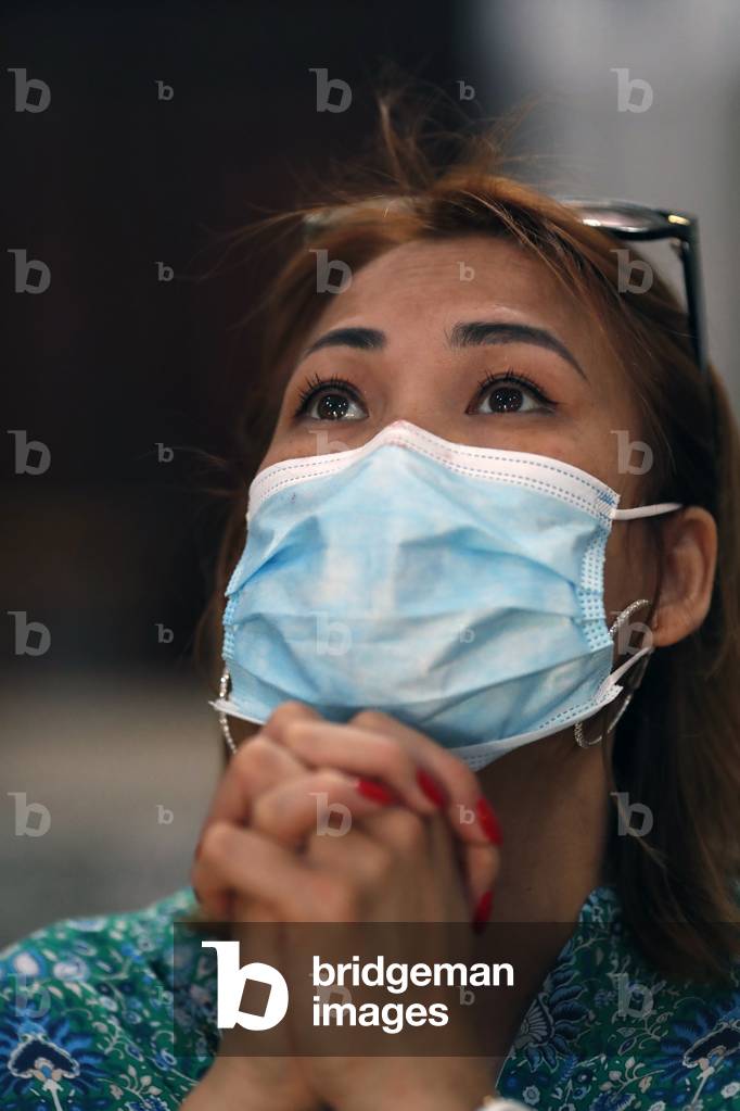 Woman with  surgical mask praying in church during coronavirus epidemic. Covid-19.