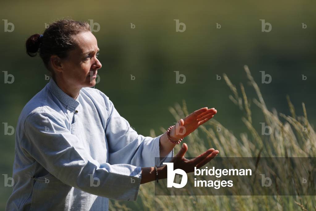 Woman practicing Qi Gong or Tai Chi exercise   in nature.  France.