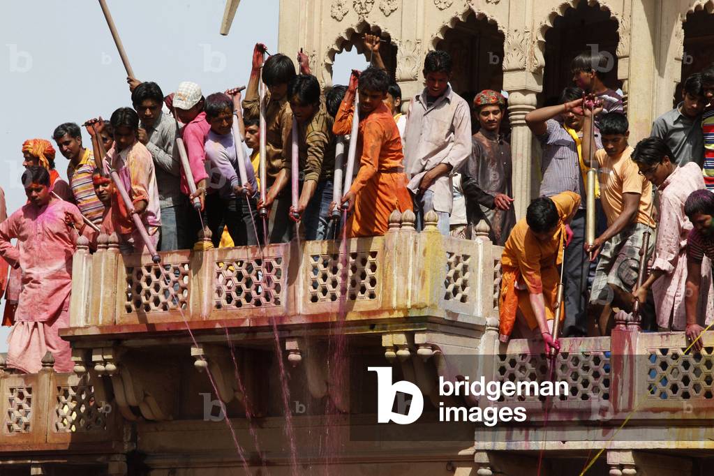Young men celebrating Holi festival by splashing colored fluids on temple visitors Nandgaon Inde